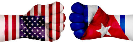 The concept of the struggle of peoples. Two hands are clenched into fists and are located opposite each other. Hands painted in the colors of the flags of the countries. Cuba vs USAの写真素材