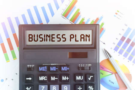 The concept of business and finance. On the table are financial charts and a calculator, on the electronic board of which is written the text - BUSINESS PLANの写真素材