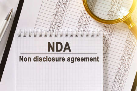 On the table are financial reports, a pen, a magnifying glass and a notebook with the inscription - NDA. Non disclosure agreement. Business and finance concept.の写真素材