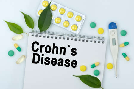 On the table are pills, a thermometer, leaves and a notebook with the inscription -Crohns Disease. The concept of medicine.の写真素材
