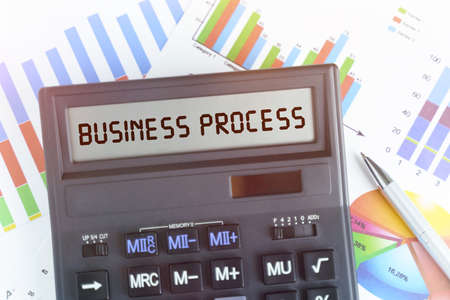 The concept of business and finance. On the table are financial charts and a calculator, on the electronic board of which is written the text - BUSINESS PROCESSの写真素材