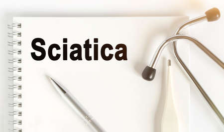 On the table are a stethoscope, a thermometer, a pen and a notebook with the inscription -Sciatica. The concept of medicine.の写真素材