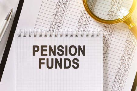 On the table are financial reports, a pen, a magnifying glass and a notebook with the inscription - PENSION FUNDS. Business and finance concept.の写真素材