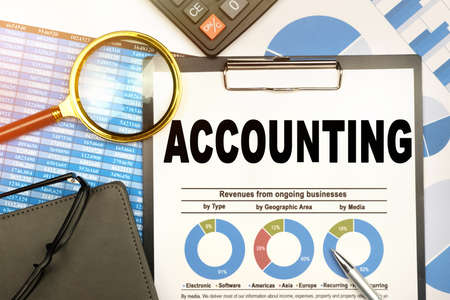 Finance and business concept. The businessman has on his desk graphs with reports, a notebook, a magnifying glass and a document with the inscription - ACCOUNTINGの写真素材