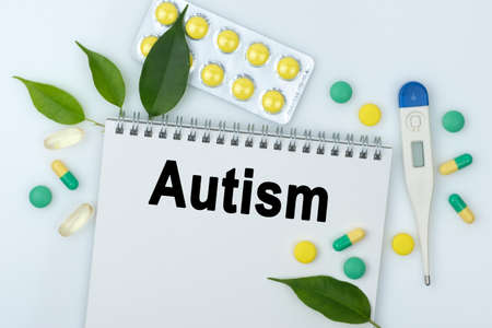 On the table are pills, a thermometer, leaves and a notebook with the inscription -Autism. The concept of medicine.の写真素材