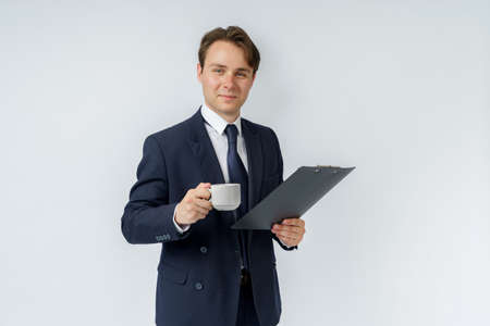 Businessman holds a cup of coffee and a tablet in his hands. White background. Business and finance conceptの写真素材