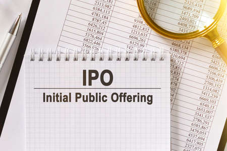 On the table are financial reports, a pen, a magnifying glass and a notebook with the inscription - IPO. Initial Public Offering. Business and finance concept.の写真素材