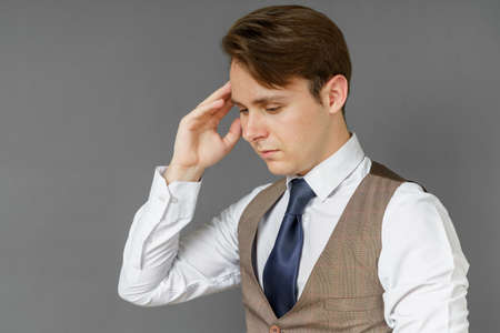An emotional portrait of a businessman who touches his head with his hands. Gray background. Business and finance conceptの写真素材
