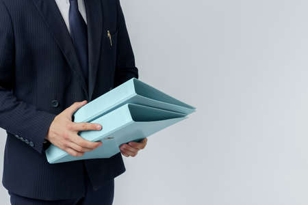 Businessman in a blue suit holds a folder in his hands on a white background. No face visible.の写真素材