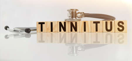 TINNITUS the word on wooden cubes, cubes stand on a reflective white surface, on cubes - a stethoscope. Medicine conceptの写真素材