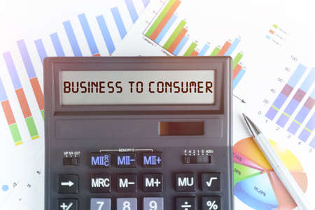 The concept of business and finance. On the table are financial charts and a calculator, on the electronic board of which is written the text - BUSINESS TO CONSUMERの写真素材