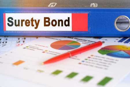 On the table are pie charts, a pen and a folder with the inscription - Surety Bond. Business and finance concept.の写真素材
