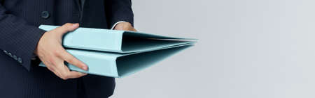 Businessman in a blue suit holds a folder in his hands on a white background. No face visible.の写真素材