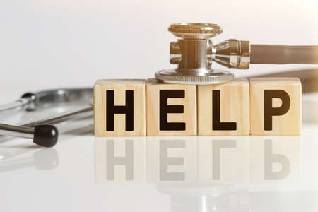 HELP the word on wooden cubes, cubes stand on a reflective white surface, on cubes - a stethoscope. Medicine conceptの写真素材