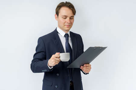 Businessman holds a cup of coffee and a tablet in his hands. White background. Business and finance conceptの写真素材