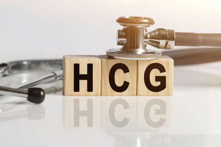 HCG the word on wooden cubes, cubes stand on a reflective white surface, on cubes - a stethoscope. Medicine conceptの写真素材