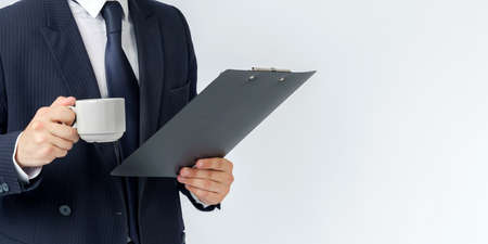 Businessman holds a cup of coffee and a tablet in his hands. White background. No face visible. Business and finance conceptの写真素材