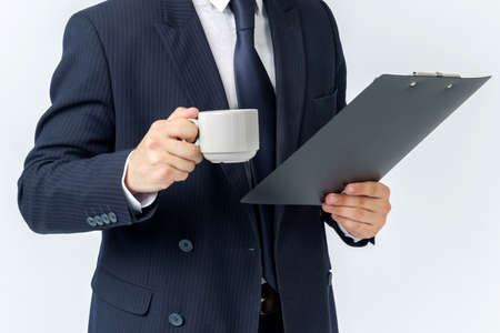 Businessman holds a cup of coffee and a tablet in his hands. White background. No face visible. Business and finance conceptの写真素材