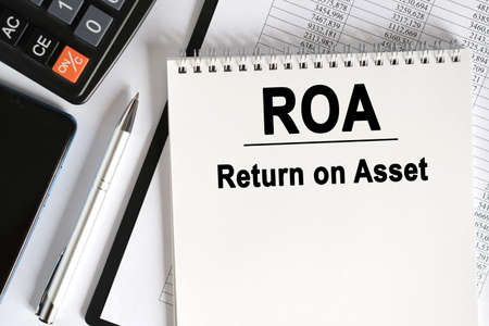 On the table lies a smartphone, a calculator and a notebook with the inscription- ROA. Return on Asset. Business conceptの写真素材