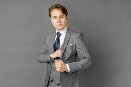 Portrait of a businessman in a suit who takes money from his inner pocket. Gray background. Business and finance conceptの写真素材