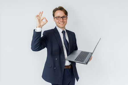 A businessman is holding a laptop, his other hand is showing OK gesture. White background. Business and finance conceptの写真素材