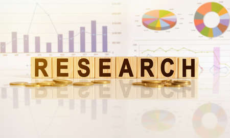 RESEARCH the word on wooden cubes, cubes stand on a reflective surface, in the background is a business diagram. Business and finance conceptの写真素材