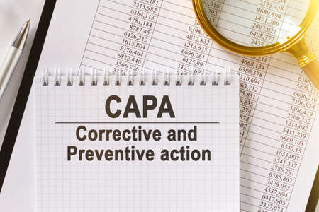 On the table are financial reports, a pen, a magnifying glass and a notebook with the inscription - CAPA. Corrective and Preventive action. Business and finance concept.の写真素材