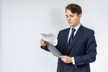 A businessman in a blue suit holds a folder in his hands and reads reports on a white background. Business and finance conceptの写真素材
