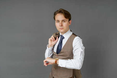 Portrait of a businessman who looks at his watch and holds a jacket over his shoulder. Gray background. Business and finance conceptの写真素材