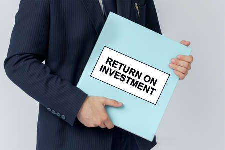 Business concept. A businessman holds a folder with documents, the text on the folder is - RETURN ON INVESTMENTの写真素材