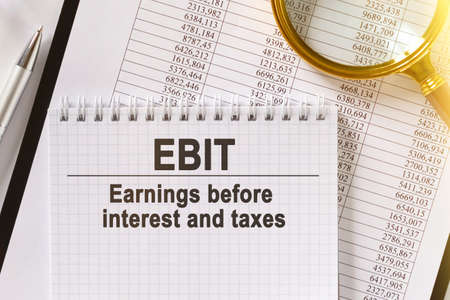 On the table are financial reports, a pen, a magnifying glass and a notebook with the inscription - EBIT. Earnings before interest and taxes. Business and finance concept.の写真素材