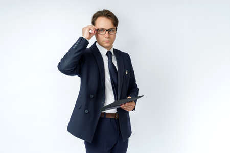 Portrait of a businessman in a blue suit who is holding an electronic tablet in his hands and adjusting his glasses. White background. Business and finance conceptの写真素材