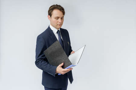 A businessman in a blue suit holds a folder in his hands and reads reports on a white background. Business and finance conceptの写真素材