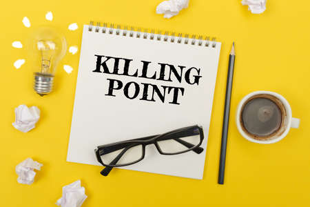Business and finance concept. On the yellow table are: a light bulb - an idea, a cup of coffee, pieces of paper, glasses and a notebook with the inscription - KILLING POINTの写真素材