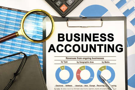 Finance and business concept. The businessman has on his desk graphs with reports, a notebook, a magnifying glass and a document with the inscription - BUSINESS ACCOUNTINGの写真素材