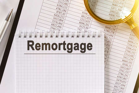 On the table are financial reports, a pen, a magnifying glass and a notebook with the inscription - remortgage. Business and finance concept.の写真素材