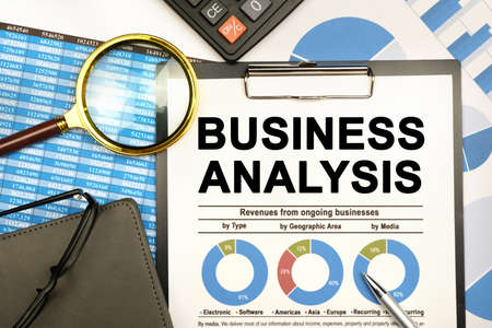 Finance and business concept. The businessman has on his desk graphs with reports, a notebook, a magnifying glass and a document with the inscription - BUSINESS ANALYSISの写真素材