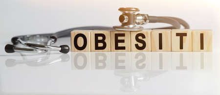 OBESITYthe word on wooden cubes, cubes stand on a reflective white surface, on cubes - a stethoscope. Medicine conceptの写真素材