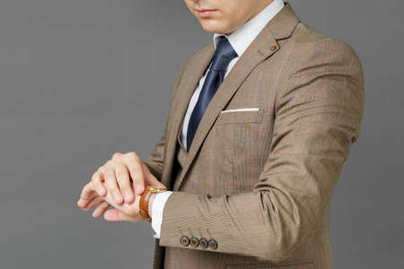 Portrait of a businessman who looks at his watch and holds a jacket over his shoulder. The face is not visible. Gray background. Business and finance conceptの写真素材