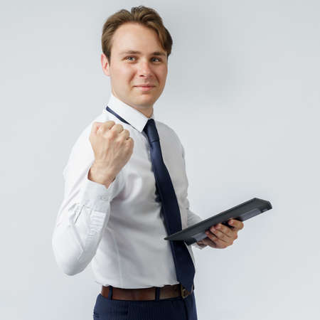 Portrait of a businessman raised his hand clenched into a fist, in the other hand an electronic tablet. White background. Business and finance conceptの写真素材