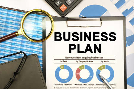 Finance and business concept. The businessman has on his desk graphs with reports, a notebook, a magnifying glass and a document with the inscription - BUSINESS PLANの写真素材