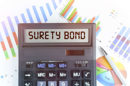 The concept of business and finance. On the table are financial charts and a calculator, on the electronic board of which is written the text - SURETY BONDの写真素材