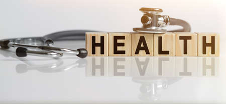 HEALTH the word on wooden cubes, cubes stand on a reflective white surface, on cubes - a stethoscope. Medicine conceptの写真素材