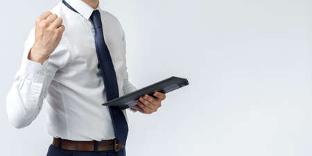 Portrait of a businessman raised his hand clenched into a fist, in the other hand an electronic tablet. No face visible. White background. Business and finance conceptの写真素材
