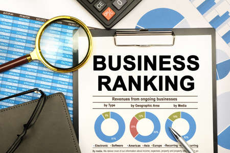 Finance and business concept. The businessman has on his desk graphs with reports, a notebook, a magnifying glass and a document with the inscription - BUSINESS RANKINGの写真素材