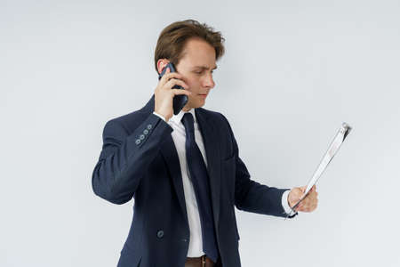 A businessman holds a tablet with reports in his hands and talks on the phone. White background. Business and finance conceptの写真素材