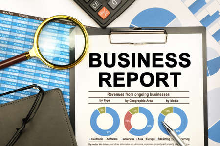 Finance and business concept. The businessman has on his desk graphs with reports, a notebook, a magnifying glass and a document with the inscription - BUSINESS REPORTの写真素材