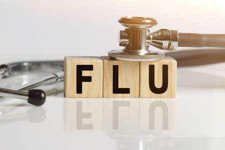 FLU the word on wooden cubes, cubes stand on a reflective white surface, on cubes - a stethoscope. Medicine conceptの写真素材