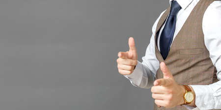 Portrait of a businessman who is making fingers gestures forward. No face visible. Gray background. Business and finance conceptの写真素材