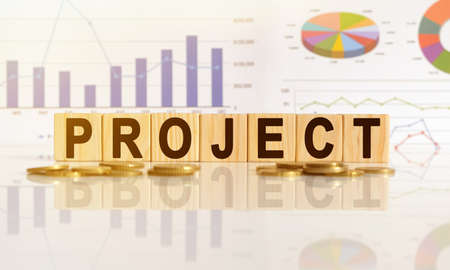 PROJECT the word on wooden cubes, cubes stand on a reflective surface, in the background is a business diagram. Business and finance conceptの写真素材